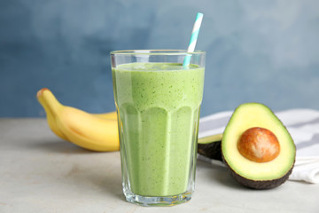 Glass of tasty smoothie and avocado on light grey table