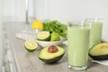 Glasses of tasty avocado smoothie and ingredients on wooden table