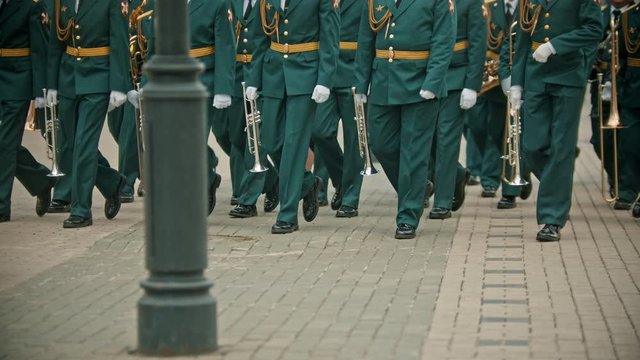A wind instrument military parade - people in green costumes walking on the street holding instruments