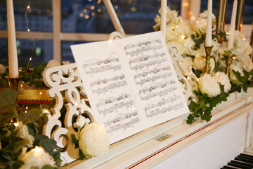 Sheet music on a white piano decorated with white flowers and candles.