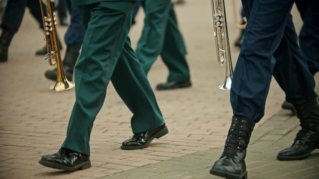 A wind instrument military parade outdoors - people in green costumes marching on the street holding instruments