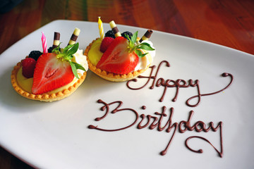 A white platter with two fruit tarts and Happy Birthday written in chocolate