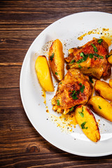 Grilled chicken thighs with baked potatoes on wooden table
