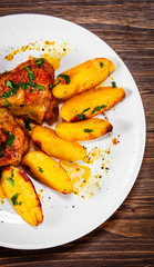 Grilled chicken thighs with baked potatoes on wooden table