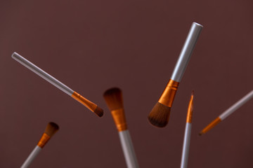 Flying cosmetic makeup brushes with white flowers on a brown background