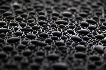 hundreds and thousands of water droplets beading on a gloss black surface of a waxed car