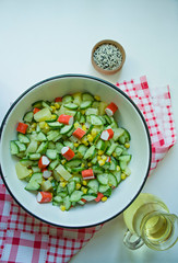 Salad with corn, crab sticks, cucumbers in a white bowl on a white background. Vegetarian salad. Cooking process.