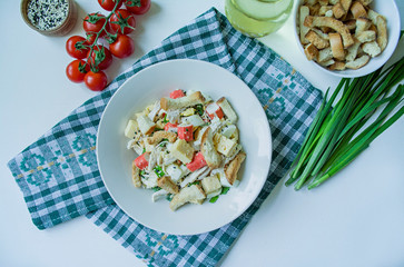 Salad with crackers, crab sticks, chicken fillet, fresh herbs and hard cheese seasoned with mayonnaise butter served in a white plate. Salad with mayonnaise. View from above. White background.