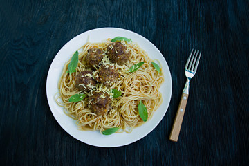 Pasta with meatballs and parsley in tomato sauce. Dark wooden background. View from above.