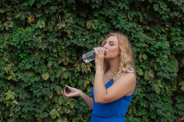 Young beautiful girl on a background of a wall of wild grapes, drinks water. Copy space.