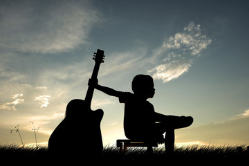 Silhouette a little boy traveling with guitar. Summer, Asian kid at the sunset, happy time,...