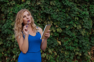 Young beautiful girl on a background of a wall of wild grapes, makes notes in a notebook, an idea has come. Copy space.