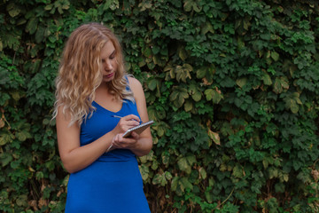Young beautiful girl on a background of a wall of wild grapes, makes notes in a notebook, an idea has come. Copy space.