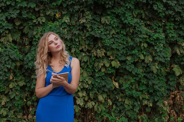 Young beautiful girl on a background of a wall of wild grapes, makes notes in a notebook, an idea has come. Copy space.