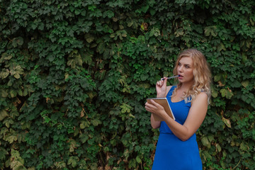 Young beautiful girl on a background of a wall of wild grapes, makes notes in a notebook, an idea has come. Copy space.