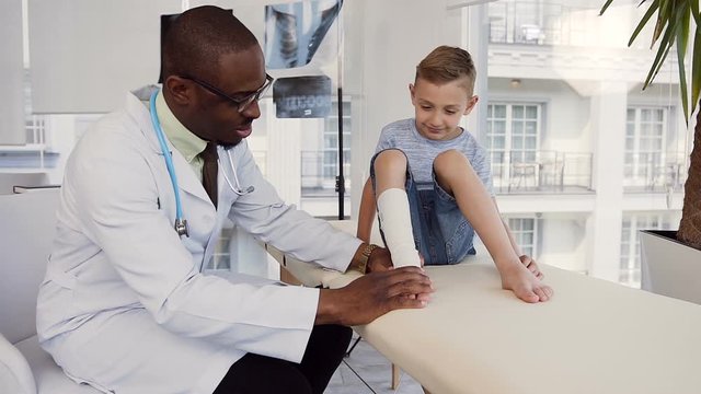 Male doctor bandaging leg of cute boy.