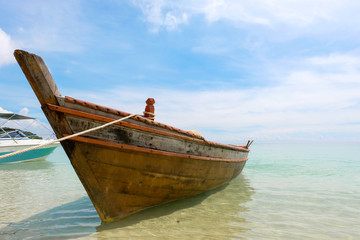 Fototapeta na wymiar Old wooden boat and blue sea under cloudy sky on white beach in sunny day.