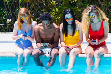 Young interracial people with mobile phones in the pool