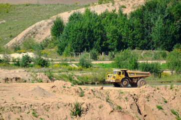 Big yellow dump truck transporting stone and gravel in an sand open-pit. Mining quarry for the production of crushed stone, sand and gravel for use in the construction industry - image