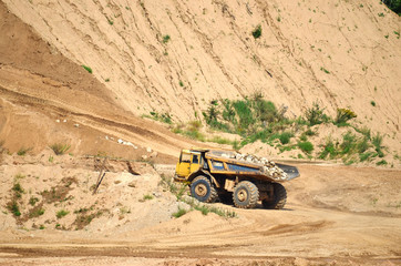 Big yellow dump truck transporting stone and gravel in an sand open-pit. Mining quarry for the production of crushed stone, sand and gravel for use in the construction industry - image