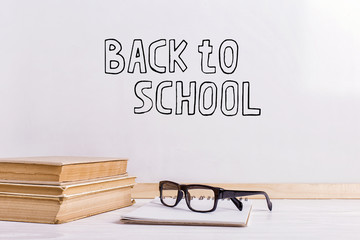The inscription marker on a white board, Back to School. A table with books and glasses.