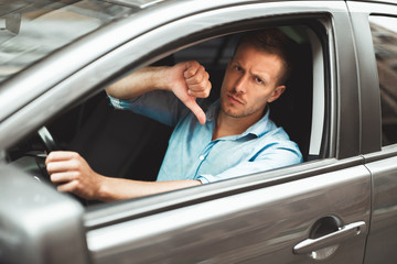 young handsome man sitting in his car showing dislike sign