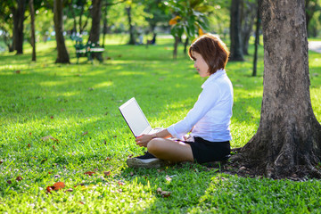 Young woman using computer on green grasses in the park. freelance working outdoor or relaxation concept.