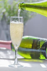 A bottle filling a glass with champagne and in the background a green bottle of unfocused champagne.