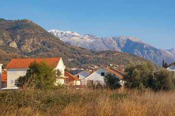 Fototapeta na wymiar Sunny winter day in Mediterranean village. Montenegro, Tivat. View of snow-capped peaks of Lovcen mountain and village of Donja Lastva