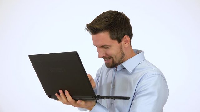 A young handsome man looks mischievously around and works on a computer - white screen studio