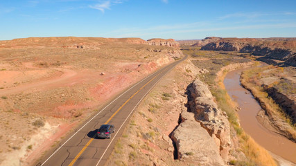 AERIAL: Black SUV car driving along the winding empty road through canyon valley