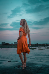 Fototapeta na wymiar Beautiful sensual woman in orange dress posing on the black sand beach during sunset