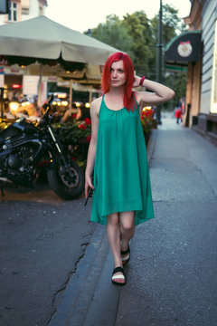Fototapeta portrait of a cheerful girl on the streets of the evening city. dressed in a green dress. Red hair. Restaurant in the background, vertical photo, historical center. Krakow Poland