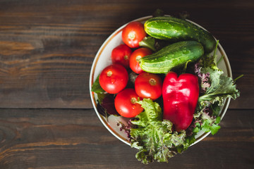 Fresh vegetables, tomatoes, cucumbers, lettuce, red peppers, and herbs in a plate on a rustic wooden table - rural style, healthy, organic food concept