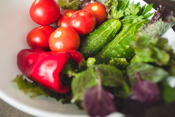 Fresh vegetables, tomatoes, cucumbers, lettuce, red peppers, and herbs in a plate on a rustic wooden table - rural style, healthy, organic food concept