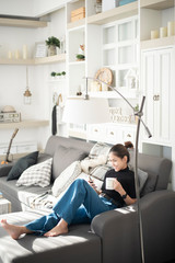 Young beautiful woman relaxing on sofa at home and using smart phone