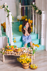 A brunette girl in a stylish polka-dot dress sits on the steps and holds an Easter egg in her hand. Decorative elements. Holiday Easter. Wicker baskets and flowers.