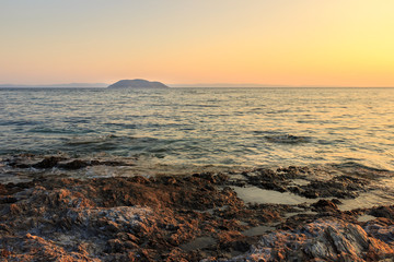 Foreground rocks and wavy sea in front of the Turtle island in Greece during sunset, viewed from the reef on Paradaisos beach in Neos Marmaras