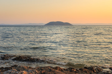 Foreground rocks and wavy sea in front of the Turtle island in Greece during sunset, viewed from the reef on Paradaisos beach in Neos Marmaras