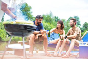 Woman preparing food in barbecue grill with friends on pier