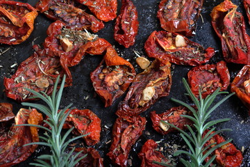 Sun-dried tomatoes with spices and garlic on a baking sheet. On top of them lies fresh rosemary.