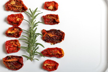 Sun-dried tomatoes with spices and garlic on a light tray. Nearby lies fresh rosemary.