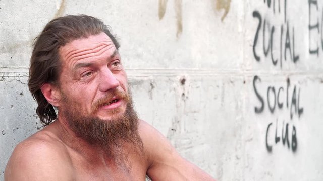 Down-and-out person talks on the camera. Homeless man looks at the camera and talks. Real person with no fixed abode