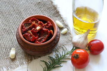 Sun-dried tomatoes with spices and garlic in a clay pot. Nearby is a bottle with olive oil, tomatoes, rosemary and garlic.