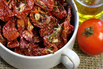 Sun-dried tomatoes with spices and garlic in a plate. Nearby is a bottle with olive oil and tomatoes.