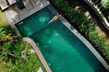 Unrecognizable woman in beige bikini relaxing in infinity pool in Bali admires a beautiful view of...