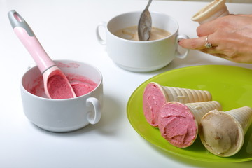 Homemade strawberry and banana ice cream. In edible horns on a plate. A woman fills the horn with ice cream.