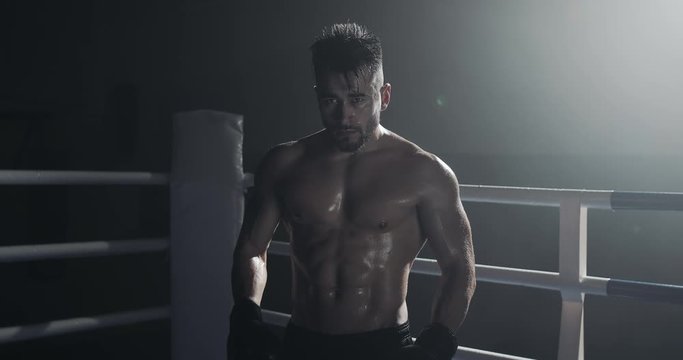 Portrait of tired male boxer standing on the boxing ring and looking intensely at the camera.