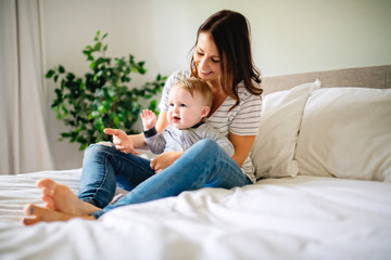 Mother and child on a white bed playing in sunny bedroom