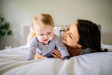 Mother and child on a white bed playing in sunny bedroom
